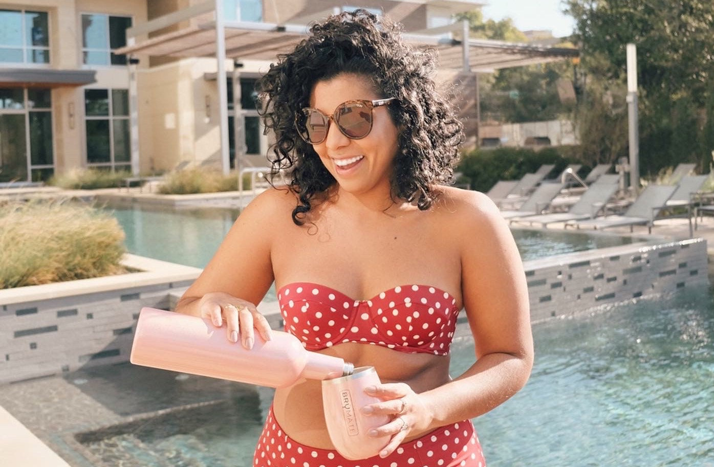 woman pouring beverage into tumbler by a pool.