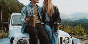 a couple sitting on the hood of a car in the mountains.